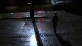 Movie still from “House of Games” (1987), directed by David Mamet – A person walking on a wet sidewalk at night; Extreme Wide shot, High angle