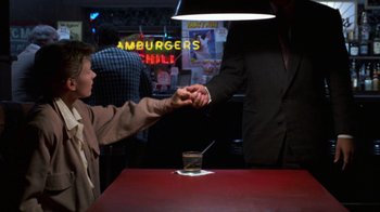 Movie still from “House of Games” (1987), directed by David Mamet – Two people shaking hands over a table at a restaurant; Medium shot, High angle