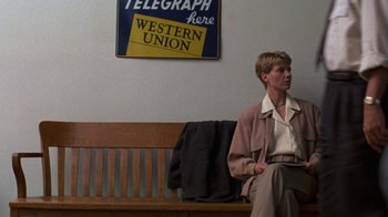 Movie still from “House of Games” (1987), directed by David Mamet – A woman sitting on a wooden bench in front of a telegraph sign; Wide shot, Low angle