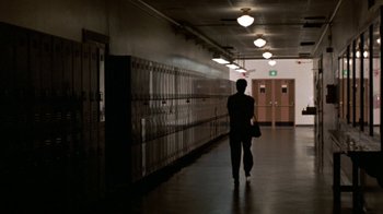 Movie still from “House of Games” (1987), directed by David Mamet – A person walking down a hallway in front of lockers; Wide shot, Low angle