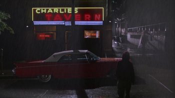 Movie still from “House of Games” (1987), directed by David Mamet – A car parked on the side of the road in front of a building; Extreme Wide shot, High angle