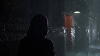Movie still from “House of Games” (1987), directed by David Mamet – A person wearing a hooded jacket standing in the rain; Wide shot, Over the shoulder angle
