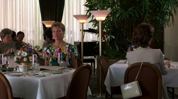 Movie still from “House of Games” (1987), directed by David Mamet – A woman sitting at a table with a glass of wine; Medium shot, Over the shoulder angle