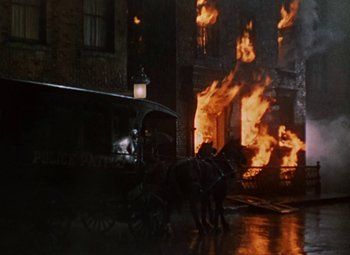Movie still from “House of Wax” (1953), directed by André De Toth – Two horses pulling a carriage in front of a burning building at night; Extreme Wide shot, Low angle