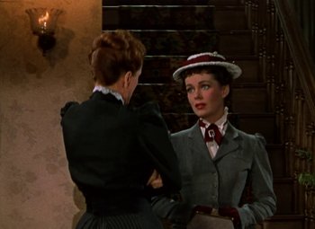 Movie still from “House of Wax” (1953), directed by André De Toth – A woman in a suit and hat talking to another woman in front of a staircase; Medium shot, Over the shoulder angle
