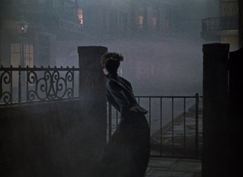 Movie still from “House of Wax” (1953), directed by André De Toth – A woman standing on a balcony in the fog; Wide shot, Low angle