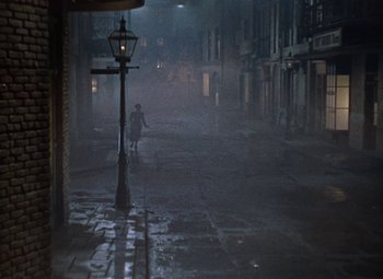 Movie still from “House of Wax” (1953), directed by André De Toth – A person walking down a street at night; Extreme Wide shot, High angle