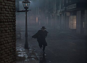Movie still from “House of Wax” (1953), directed by André De Toth – A man running down the street in the rain; Wide shot, High angle