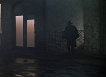 Movie still from “House of Wax” (1953), directed by André De Toth – A man standing in a dark room next to a brick wall; Wide shot, Low angle