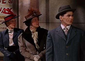 Movie still from “House of Wax” (1953), directed by André De Toth – A man and two women wearing hats and suits; Medium shot, Low angle