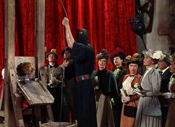Movie still from “House of Wax” (1953), directed by André De Toth – A group of people standing in front of a man holding a sword; Wide shot, Low angle