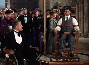 Movie still from “House of Wax” (1953), directed by André De Toth – A painting of william kemmler sitting in a chair; Wide shot, Over the shoulder angle