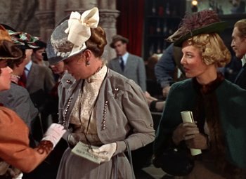 Movie still from “House of Wax” (1953), directed by André De Toth – Two women in fancy hats are standing next to each other; Medium shot, Over the shoulder angle