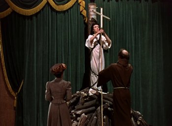 Movie still from “House of Wax” (1953), directed by André De Toth – A man holding a cross on top of a pile of wood; Wide shot, Low angle