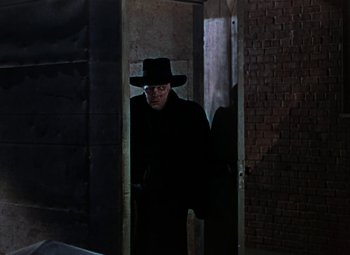 Movie still from “House of Wax” (1953), directed by André De Toth – A man wearing a black hat and a black coat; Medium shot, Low angle