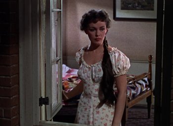 Movie still from “House of Wax” (1953), directed by André De Toth – A woman standing in front of a window in a room; Medium shot, Over the shoulder angle