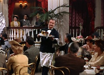 Movie still from “House of Wax” (1953), directed by André De Toth – A man holding a tray of food in front of people; Wide shot, Low angle