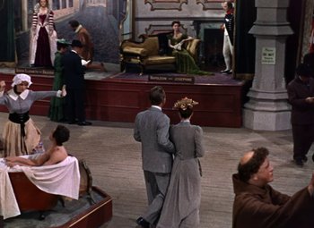 Movie still from “House of Wax” (1953), directed by André De Toth – A couple of people that are standing in a room; Wide shot, High angle