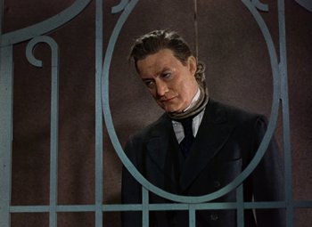 Movie still from “House of Wax” (1953), directed by André De Toth – A man standing in front of an iron gate; Medium shot, Low angle
