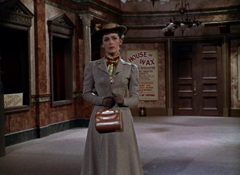 Movie still from “House of Wax” (1953), directed by André De Toth – A woman in a gray coat and hat holding a purse; Wide shot, Low angle