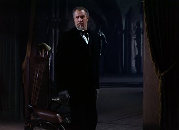 Movie still from “House of Wax” (1953), directed by André De Toth – A man in a suit and bow tie standing next to a chair; Wide shot, Low angle