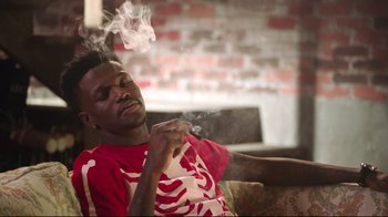 Movie still from “How High 2” (2019), directed by Bruce Leddy – A man sitting on a couch smoking a cigarette; Medium shot, Low angle