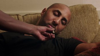 Movie still from “How High 2” (2019), directed by Bruce Leddy – A man smoking a cigarette while lying on a couch; Medium shot, Low angle