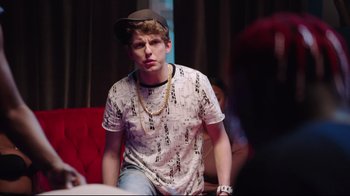 Movie still from “How High 2” (2019), directed by Bruce Leddy – A young man wearing a hat sitting on top of a red chair; Medium shot, Over the shoulder angle