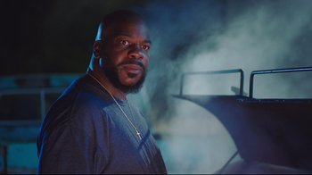 Movie still from “How High 2” (2019), directed by Bruce Leddy – A man with a beard is standing in front of a grill; Medium shot, Low angle