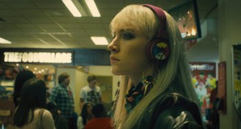 Movie still from “How I Live Now” (2013), directed by Kevin Macdonald – A woman with blonde hair wearing headphones in an airport; Close Up shot, Over the shoulder angle