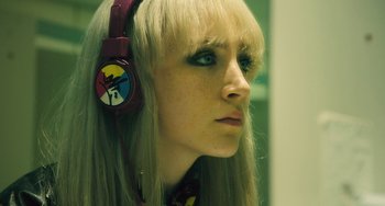 Movie still from “How I Live Now” (2013), directed by Kevin Macdonald – A woman with blonde hair wearing a pair of headphones; Close Up shot, High angle