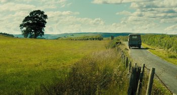 Movie still from “How I Live Now” (2013), directed by Kevin Macdonald – A car driving down a road near a grassy field; Extreme Wide shot, Low angle