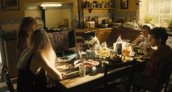 Movie still from “How I Live Now” (2013), directed by Kevin Macdonald – A woman and a dog in a kitchen with food on the table; Wide shot, High angle