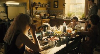 Movie still from “How I Live Now” (2013), directed by Kevin Macdonald – Two people sitting at a table with food on top of it; Medium shot, High angle