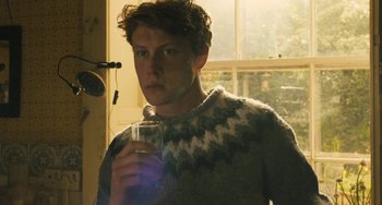 Movie still from “How I Live Now” (2013), directed by Kevin Macdonald – A young man holding a glass of water in front of a window; Close Up shot, Low angle