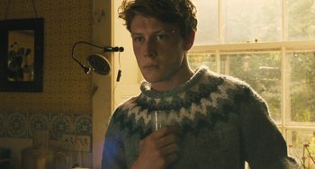 Movie still from “How I Live Now” (2013), directed by Kevin Macdonald – A young man holding a wine glass while standing in front of a window; Close Up shot, Low angle