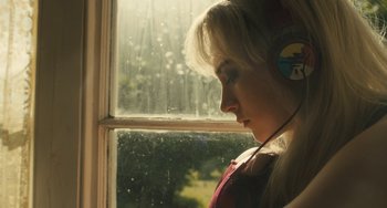 Movie still from “How I Live Now” (2013), directed by Kevin Macdonald – A woman wearing headphones looking out a window; Close Up shot, High angle