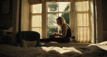 Movie still from “How I Live Now” (2013), directed by Kevin Macdonald – A woman sitting on a bed looking out of a window; Wide shot, High angle