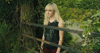 Movie still from “How I Live Now” (2013), directed by Kevin Macdonald – A woman standing in front of a tree and a fence; Medium shot, High angle