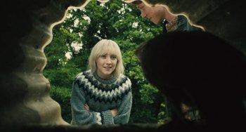 Movie still from “How I Live Now” (2013), directed by Kevin Macdonald – A woman wearing a sweater standing in front of a tree; Medium shot, Over the shoulder angle
