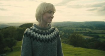 Movie still from “How I Live Now” (2013), directed by Kevin Macdonald – A woman standing on top of a grass covered hill; Close Up shot, Over the shoulder angle