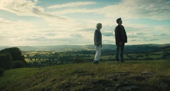Movie still from “How I Live Now” (2013), directed by Kevin Macdonald – Two people standing on top of a grassy hill; Wide shot, Low angle