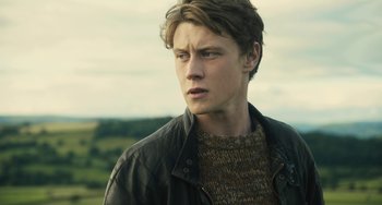 Movie still from “How I Live Now” (2013), directed by Kevin Macdonald – A young man wearing a brown sweater and a leather jacket; Close Up shot, Low angle