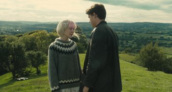 Movie still from “How I Live Now” (2013), directed by Kevin Macdonald – A man and a woman standing on top of a green hill; Medium shot, Over the shoulder angle