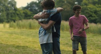 Movie still from “How I Live Now” (2013), directed by Kevin Macdonald – A group of young men hugging in a field; Medium shot, Over the shoulder angle