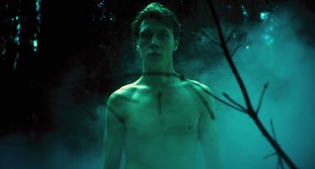 Movie still from “How I Live Now” (2013), directed by Kevin Macdonald – A shirtless man standing in the middle of a forest; Medium shot, Low angle