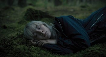Movie still from “How I Live Now” (2013), directed by Kevin Macdonald – A woman is laying on the ground with her eyes closed; Medium shot, High angle
