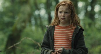 Movie still from “How I Live Now” (2013), directed by Kevin Macdonald – A girl with red hair is standing in the woods; Medium shot, Low angle