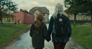 Movie still from “How I Live Now” (2013), directed by Kevin Macdonald – Two people walking down a street holding hands; Medium shot, Over the shoulder angle