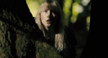 Movie still from “How I Live Now” (2013), directed by Kevin Macdonald – A woman with long blonde hair standing next to a tree; Close Up shot, Low angle